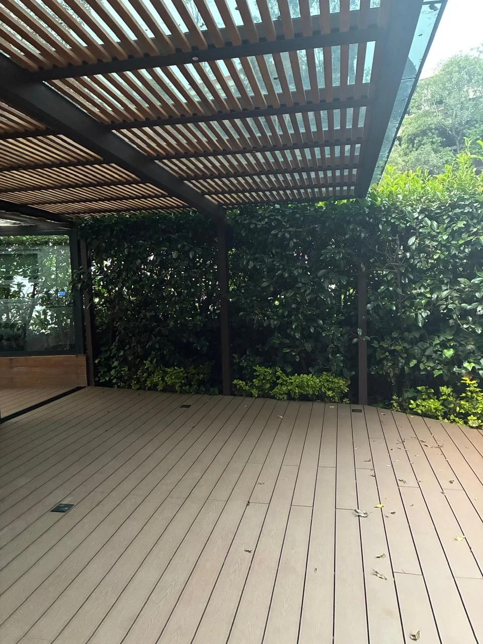 Pérgola de madera y vidrio junto a un muro cubierto de vegetación